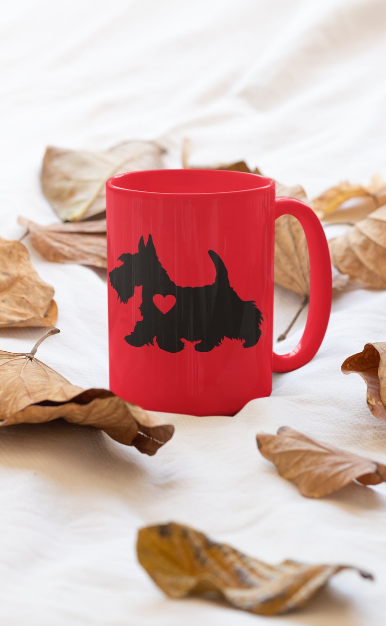 May include: A red ceramic mug with a black silhouette of a Scottish Terrier with a red heart on its chest. The mug is surrounded by brown leaves on a white background.