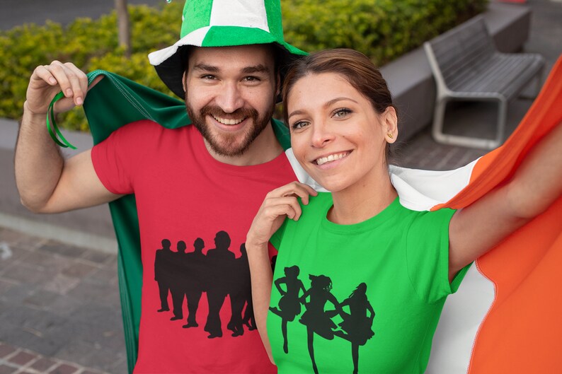 May include: Two people wearing red and green t-shirts with silhouettes of Irish dancers and musicians. They are holding an Irish flag.