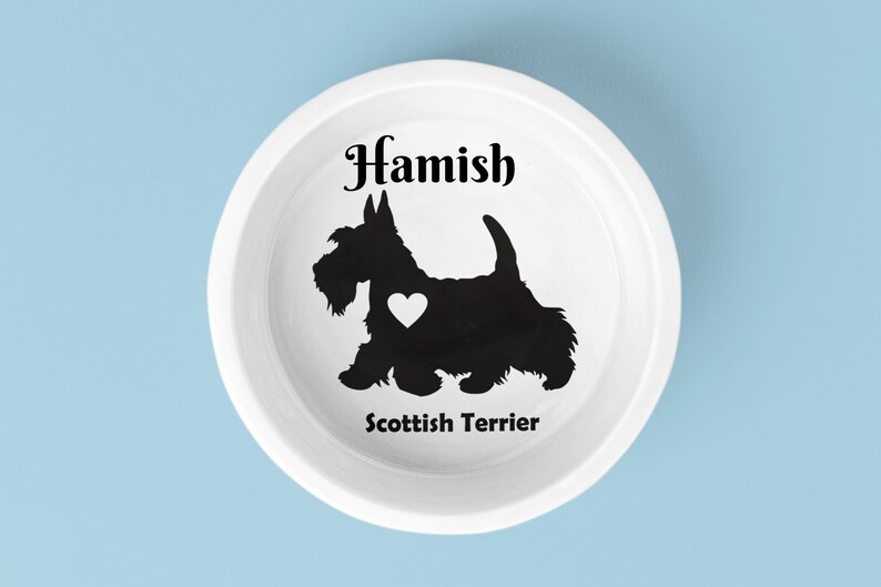 May include: White ceramic dog bowl with a black silhouette of a Scottish Terrier with a heart on its chest. The bowl is personalized with the name "Hamish" and the breed "Scottish Terrier".