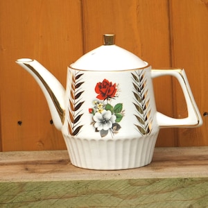 May include: White teapot with a gold trim and floral design featuring red and white roses. The teapot has a lid and a handle.