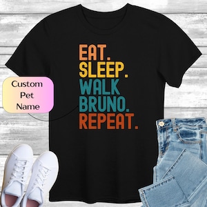 May include: Black t-shirt with a vintage-style graphic that reads "Eat. Sleep. Walk [Pet Name]. Repeat."