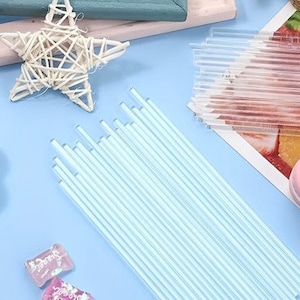 May include: A bundle of clear plastic straws, approximately 30 in total, arranged in a fan shape on a light blue surface. The straws are about 25 cm long and are perfect for crafting or decorating.