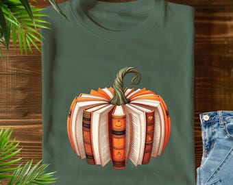 Könnte beinhalten: Grünes T-Shirt mit einem Kürbisdesign aus Büchern. Der Kürbis ist orange und weiß mit einem grünen Stiel. Die Bücher haben orangefarbene und braune Buchrücken. Das T-Shirt liegt auf einer Holzoberfläche.