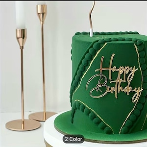 Può includere: Una torta verde con dettagli dorati e un topper dorato 'Buon compleanno'. La torta è su un supporto per torte bianco.