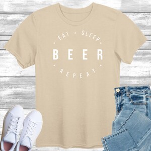 May include: A beige t-shirt with a white graphic that reads "Eat. Sleep. Beer. Repeat."