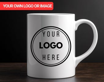 May include: A white ceramic mug featuring a black circular design with the text "YOUR LOGO HERE". The mug has a curved handle and is set against a dark background. A red banner at the top reads "YOUR OWN LOGO OR IMAGE".