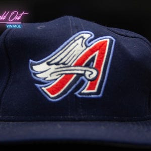 May include: A navy blue baseball cap with a red, white and blue embroidered logo of a stylised 'A' with wings. The logo is centred on the front of the cap.