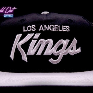 Op de afbeelding: Zwarte en witte baseballpet van de Los Angeles Kings met een witte klep. De pet heeft een wit geborduurd logo met de woorden "Los Angeles Kings" op de voorkant.