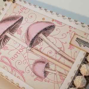 May include: A pink and white scrapbook with a decorative mushroom design and the word "Hotdog" printed on the cover. The scrapbook has a white tassel trim and a pink tag with the number "1" on it.