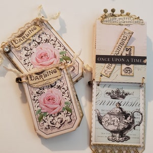 May include: A set of three vintage-style paper tags with floral designs and the words "Darling" and "Once Upon A Time". The tags are decorated with lace, ribbons, and gold accents.