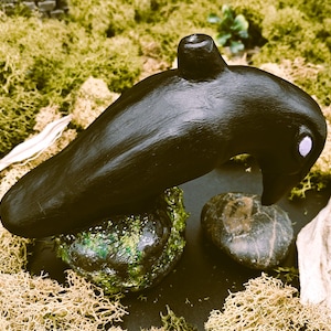 Peut inclure: Sculpture de corbeau noir avec un œil violet, perchée sur un rocher vert et brun. Le corbeau est en argile et a une finition lisse et mate.