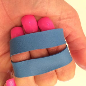 May include: Two blue rubber bands are wrapped around a person's fingers. The rubber bands are about 1 inch wide. The person's fingernails are painted pink.