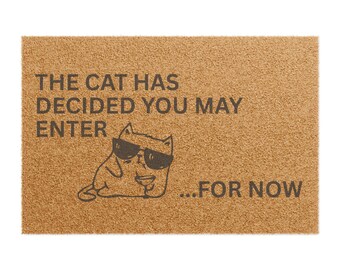 May include: A brown coir doormat with the text "The cat has decided you may enter...for now" and a cartoon cat wearing sunglasses and holding a martini glass.