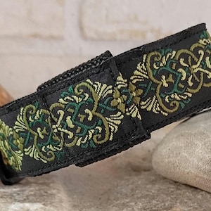 Könnte beinhalten: Ein schwarzes Stoffband mit einem komplizierten Stickmuster in Olivgrün, Waldgrün und Gold. Das Band hat eine rechteckige Form mit einem sichtbaren Klettverschluss auf der Vorderseite des Materials.