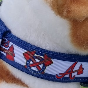 May include: A blue and white dog collar with the Atlanta Braves logo and tomahawk design. The collar has a black buckle.