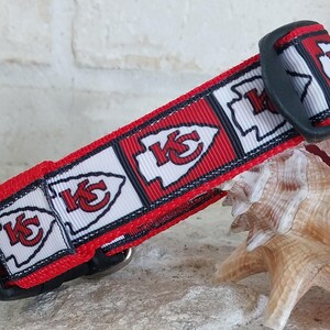 May include: Red, white and black dog collar with a repeating pattern of the Kansas City Chiefs logo. The collar has a black plastic buckle.