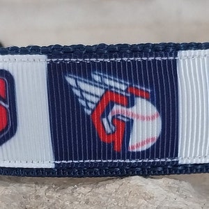 Puede incluir: Un collar para perro azul y blanco con el logotipo de los Cleveland Guardians. El logotipo presenta un "Guardians" rojo con una pelota de béisbol y alas.