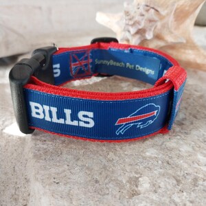 May include: Blue and red dog collar with the Buffalo Bills logo and the text "BILLS" in white. The collar has a black plastic buckle and the text "SunnyBeach Pet Designs" on the back.