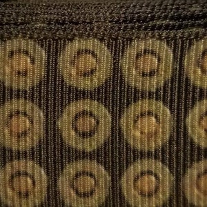 Puede incluir: Tela estampada en negro y marrón con un diseño de círculos repetidos. Los círculos tienen un centro marrón y un contorno negro.