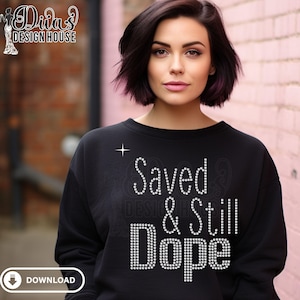 Puede incluir: Sudadera negra con el texto "Saved & Still Dope" en pedrería blanca. Una pequeña estrella está encima de la palabra "Saved". La sudadera la lleva una persona con pelo oscuro.