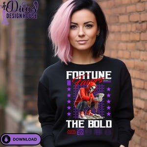 Puede incluir: Sudadera negra con el texto "FORTUNE FAVORS THE BOLD" y un gráfico de un esqueleto con una sudadera con capucha roja sosteniendo dinero. El diseño incluye estrellas moradas y un patrón de cuadrícula. Llevada por una persona con cabello rosa y negro.