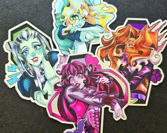 May include: Four colorful stickers featuring characters from the Monster High franchise. The stickers are shaped like coffins and feature the characters Frankie Stein, Lagoona Blue, Clawdeen Wolf, and Draculaura. Each sticker has a unique design and color scheme.