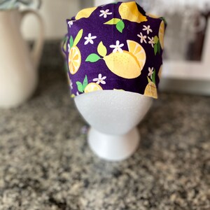 May include: Purple scrub hat with a lemon and flower pattern.