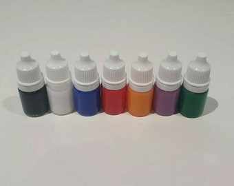 May include: Eight small bottles of paint with white dropper caps. The bottles are arranged in a row from left to right: black, white, blue, red, orange, purple, green.