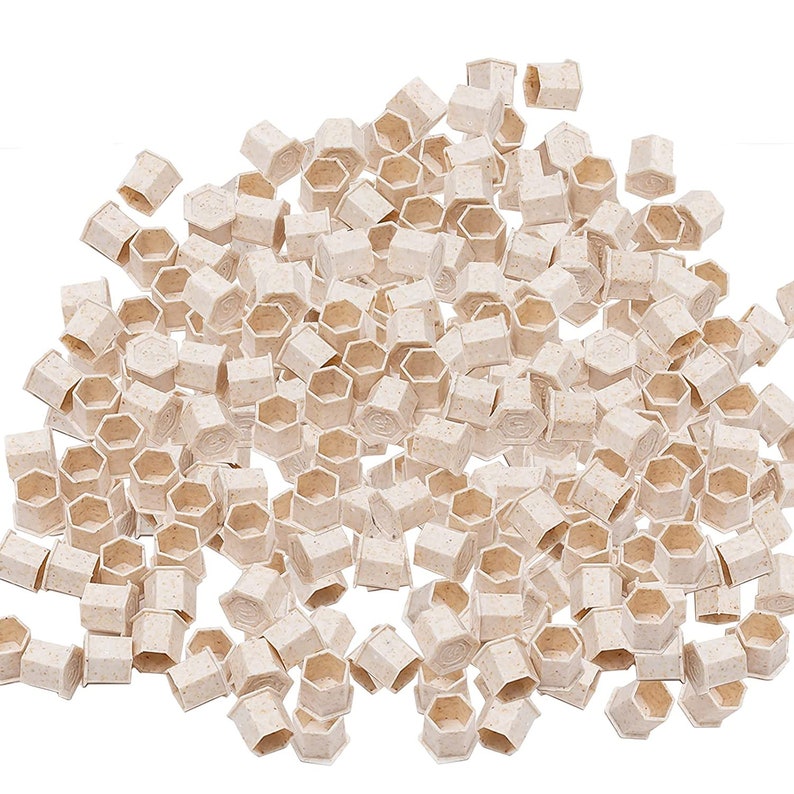 May include: A large pile of small, beige, hexagonal-shaped plastic containers. The containers are made of a textured material and have a slightly raised lip around the top edge.