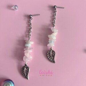 May include: A pair of silver earrings with a delicate chain and a leaf charm. Each earring features a cluster of pastel pink, blue, and white stones.