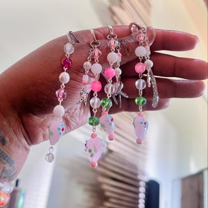 May include: Five pink, white, and green beaded keychains with silver charms. Each keychain features a pink glass charm with floral designs.