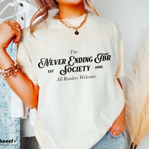 K&ouml;nnte beinhalten: Ein wei&szlig;es T-Shirt mit schwarzem Text, der "The Never Ending TBR Society Est 1995 All Readers Welcome" lautet.