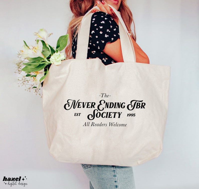 K&ouml;nnte beinhalten: Eine wei&szlig;e Canvas-Tragetasche mit schwarzem Text, der "The Never Ending TBR Society Est 1995 All Readers Welcome" lautet.
