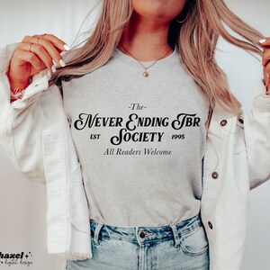K&ouml;nnte beinhalten: Ein graues T-Shirt mit schwarzem Text, der "The Never Ending TBR Society Est 1995 All Readers Welcome" lautet.