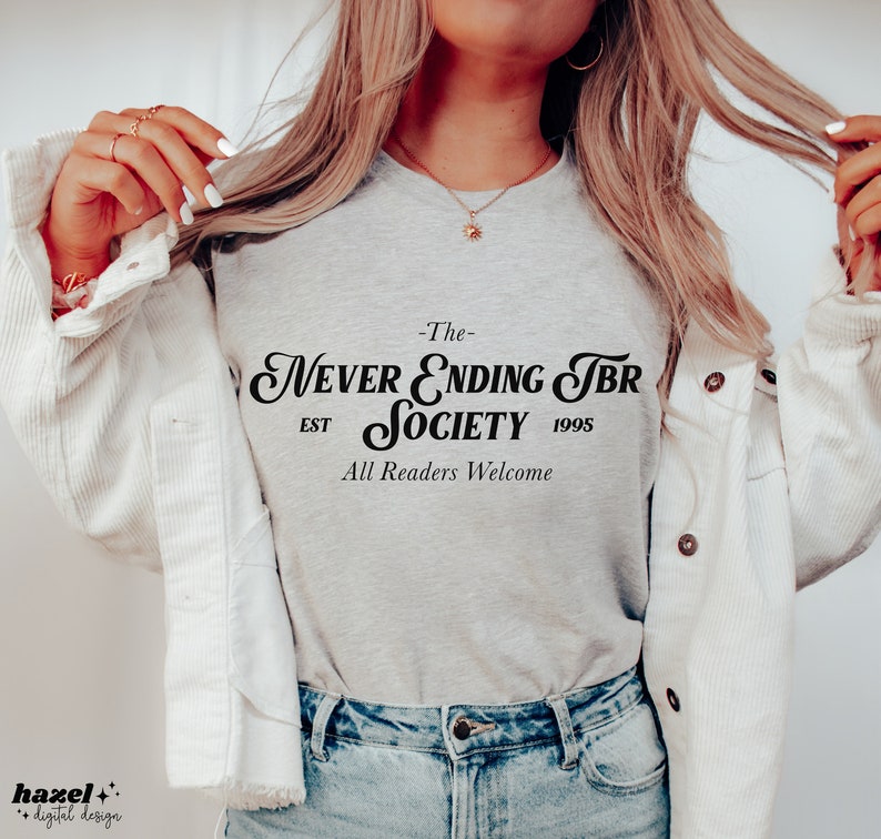 K&ouml;nnte beinhalten: Ein graues T-Shirt mit schwarzem Text, der "The Never Ending TBR Society Est 1995 All Readers Welcome" lautet.