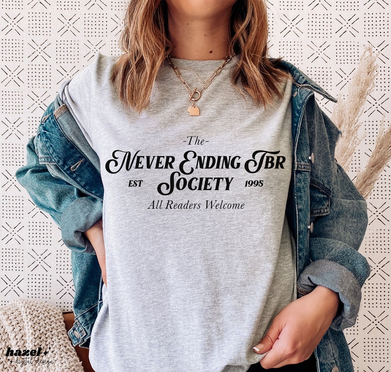 K&ouml;nnte beinhalten: Graues T-Shirt mit dem Text "The Never Ending TBR Society Est 1995 All Readers Welcome" in Schwarz.