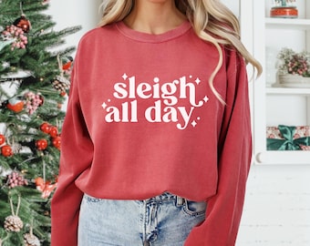 Könnte beinhalten: Ein rotes Sweatshirt mit Rundhalsausschnitt und dem weißen Schriftzug "sleigh all day" in stilisierter Schrift auf der Vorderseite, verziert mit kleinen vierzackigen Sternen. Das Kleidungsstück hat lange Ärmel sowie gerippte Bündchen am Kragen.