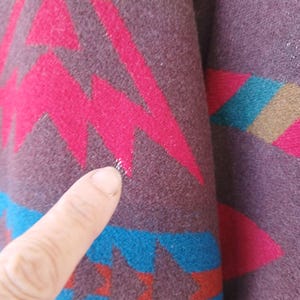 Puede incluir: Primer plano de una secci&oacute;n de tela estampada. La tela es de color p&uacute;rpura oscuro con un dise&ntilde;o geom&eacute;trico en tonos rosa, turquesa y beige. El dise&ntilde;o incluye zigzags y formas de estrella. La tela parece ser un material tejido.