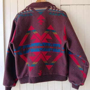 Puede incluir: Chaqueta de lana burdeos con un estampado geom&eacute;trico en rojo, azul y turquesa. La chaqueta tiene cuello y pu&ntilde;os y dobladillo de canal&eacute;. El dise&ntilde;o est&aacute; centrado en la espalda y los hombros.
