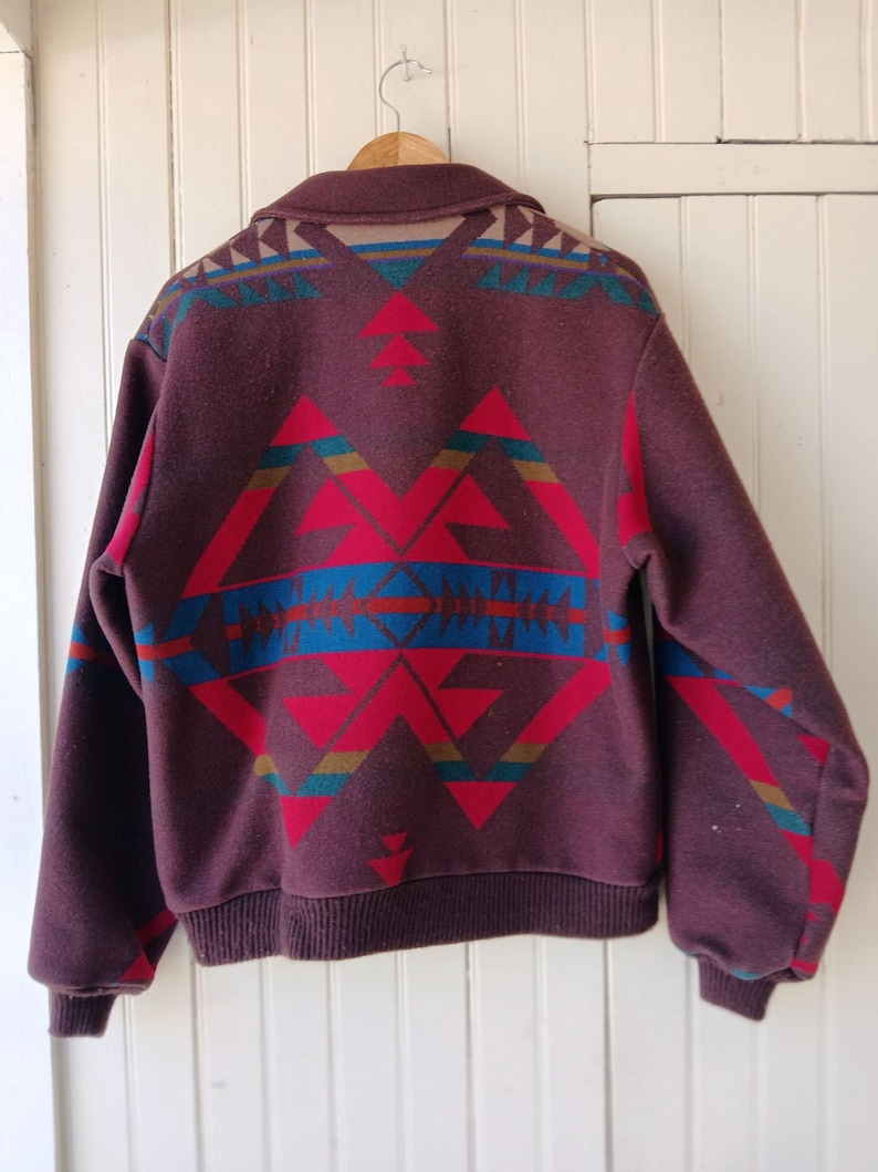 Puede incluir: Chaqueta de lana burdeos con un estampado geom&eacute;trico en rojo, azul y turquesa. La chaqueta tiene cuello y pu&ntilde;os y dobladillo de canal&eacute;. El dise&ntilde;o est&aacute; centrado en la espalda y los hombros.