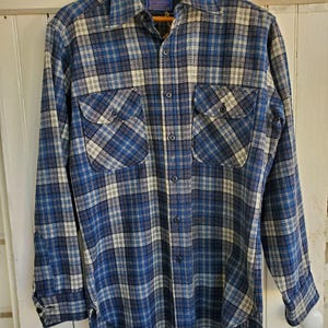 May include: A blue, white and black plaid flannel shirt with long sleeves and two chest pockets. The shirt has a button-down collar and a button front.