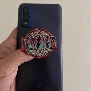 May include: A black phone with a leopard print sticker that says "MAMA" with a lightning bolt in the middle.
