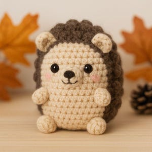 May include: A handmade crochet hedgehog in tan, brown, and black. The adorable stuffed animal has a round body, small arms and legs, and a smiling face with rosy cheeks. The hedgehog is a cute, whimsical toy.
