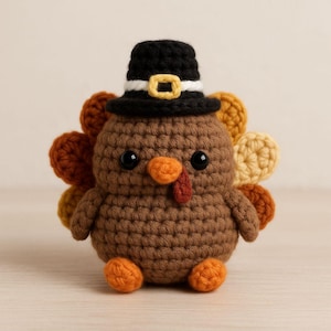 May include: A handmade crochet turkey figurine, perfect for Thanksgiving. The brown turkey has a black pilgrim hat with a yellow buckle, orange feet and beak, and a red wattle. The turkey's tail feathers are in shades of brown and yellow.