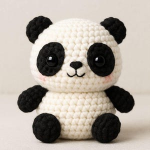 May include: A handmade crochet panda bear with a white body, black accents, and black button eyes. The panda has black ears, arms, and legs. The panda's cheeks are lightly blushed. This soft toy is perfect for children.