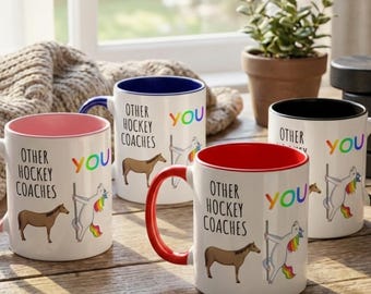 May include: Four white ceramic mugs with coloured interiors and handles. Each mug features the text "OTHER HOCKEY COACHES YOU" with a horse and a unicorn illustration. The mugs are on a wooden surface.