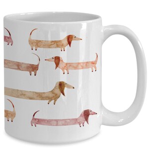 May include: White ceramic coffee mug with a pattern of brown and pink dachshund dogs. The dogs are illustrated in a watercolor style.