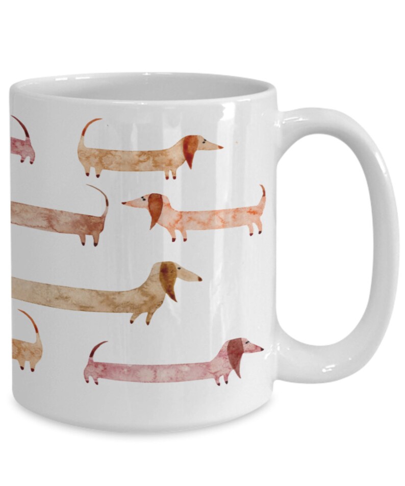 May include: White ceramic coffee mug with a pattern of brown and pink dachshund dogs. The dogs are illustrated in a watercolor style.