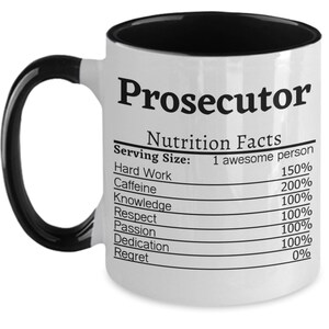May include: White ceramic coffee mug with a black interior and handle. The mug features a black and white graphic of a nutrition facts label with the title "Prosecutor". The label lists the following: Hard Work, Caffeine, Knowledge, Respect, Passion, Dedication, and Regret. Each item has a percentage next to it.