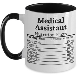 May include: White ceramic mug with a black handle and interior. The mug features the text "Medical Assistant" above a "Nutrition Facts" label. The label lists ingredients like "Hard Work" and "Caffeine" with percentage values.
